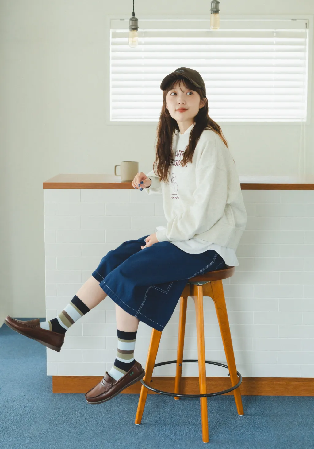 カウンターのスツールに腰掛ける大島花菜。カラフルボーダーソックスを履いている